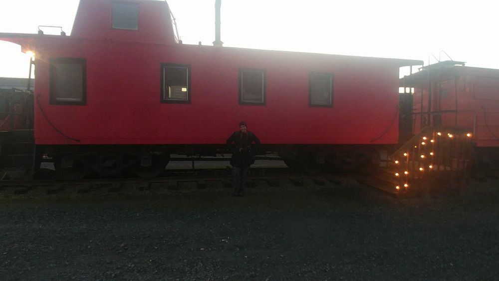 Red vintage caboose decorated with string lights at twilight.