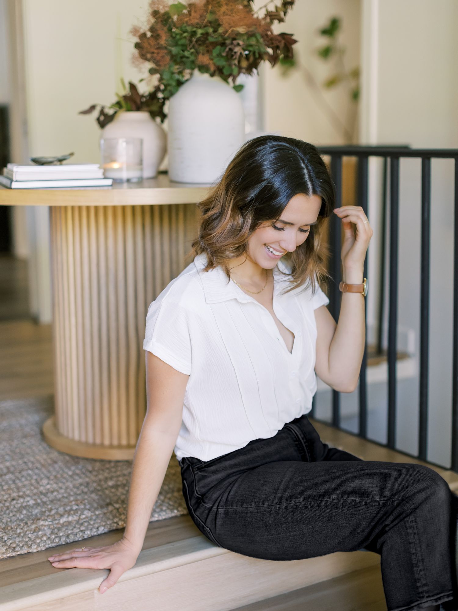 Casual portrait on stairs with white shirt and black jeans in modern interior setting.