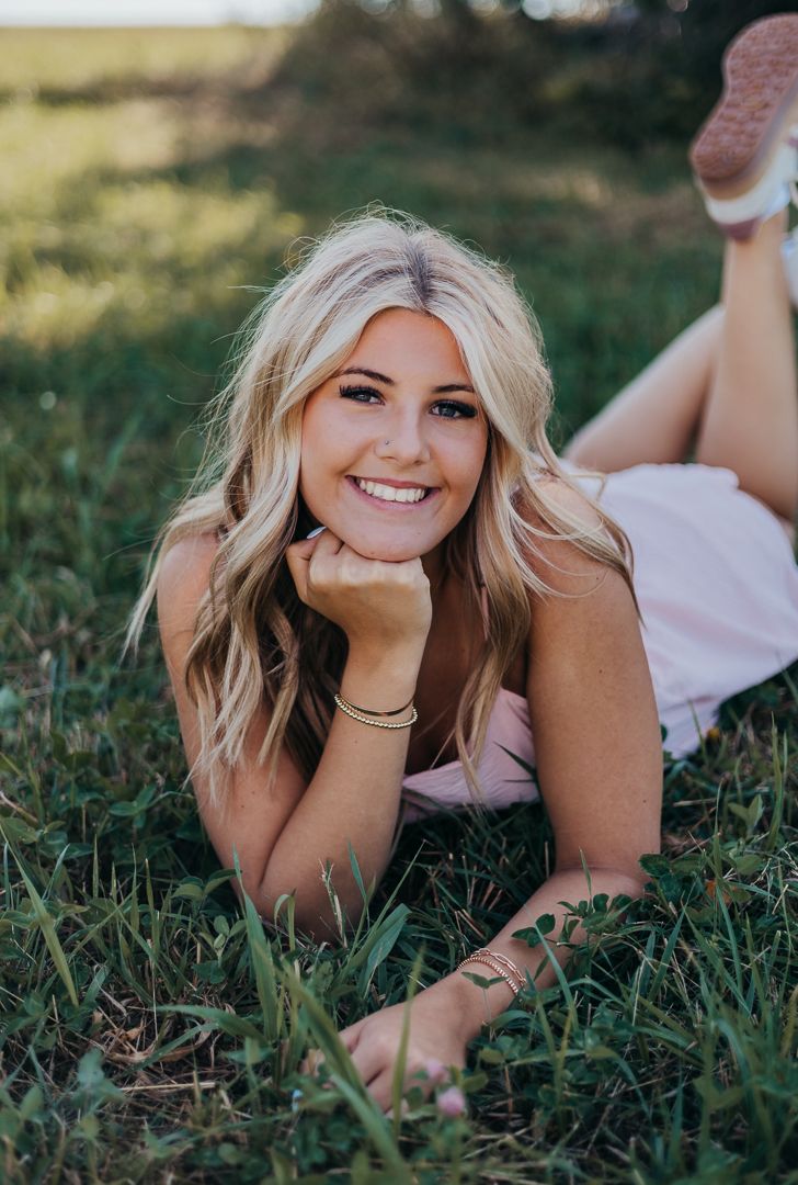 Person with blonde hair lying in grass wearing casual attire during an outdoor photo session.