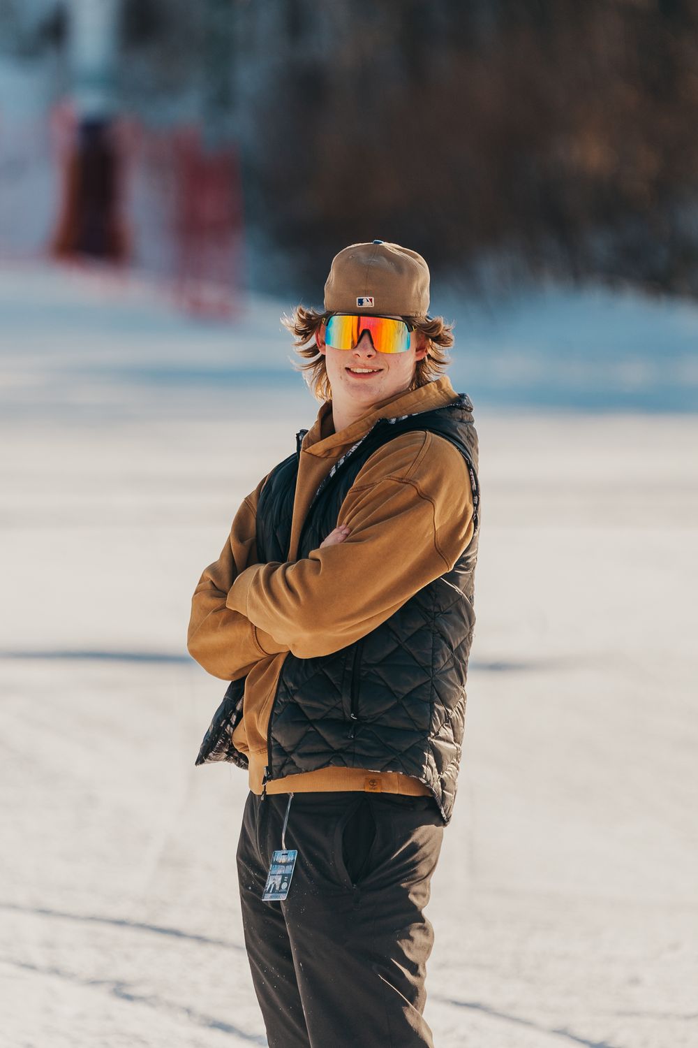 A person in winter gear takes photos on a snowy slope wearing brown and black outerwear with reflective goggles.