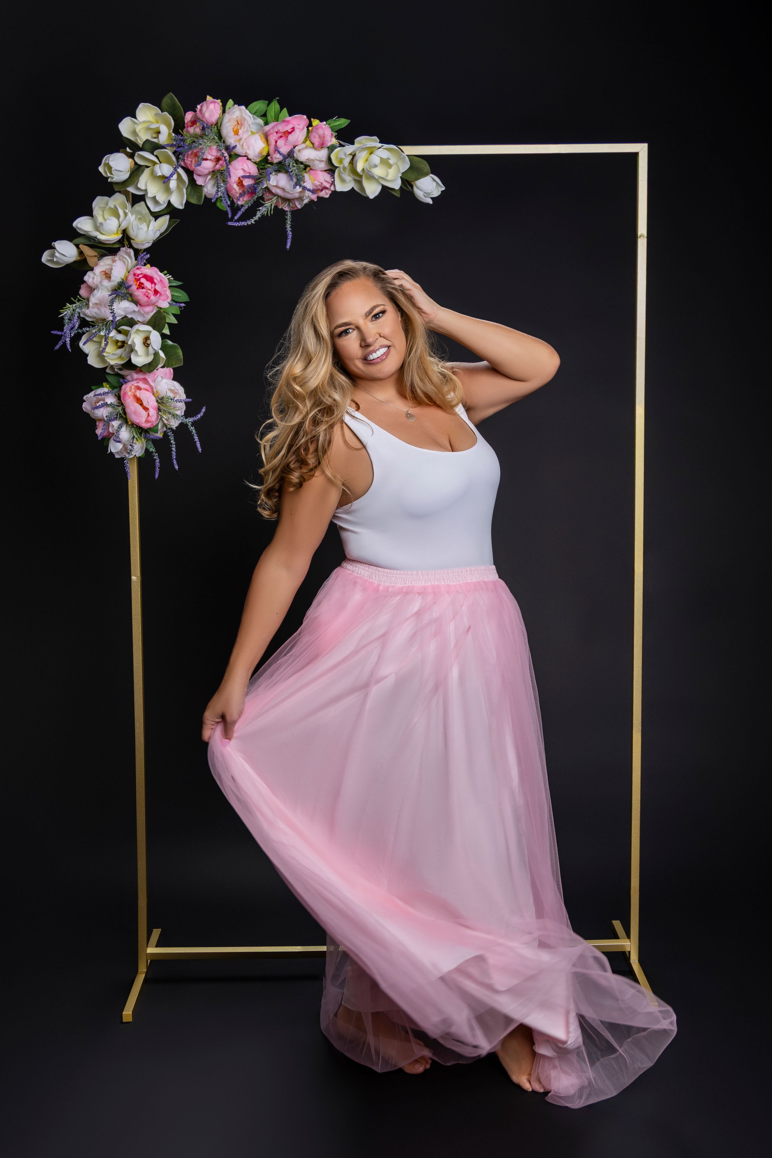Elegant plus size tulle skirt photoshoot featuring white top and flowing pink tulle skirt against black background.