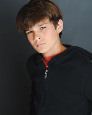 Studio portrait of figure in black sweater against grey background with dramatic side lighting.