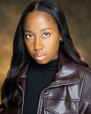 Young woman in burgundy leather jacket and black turtleneck poses for professional headshot photo.
