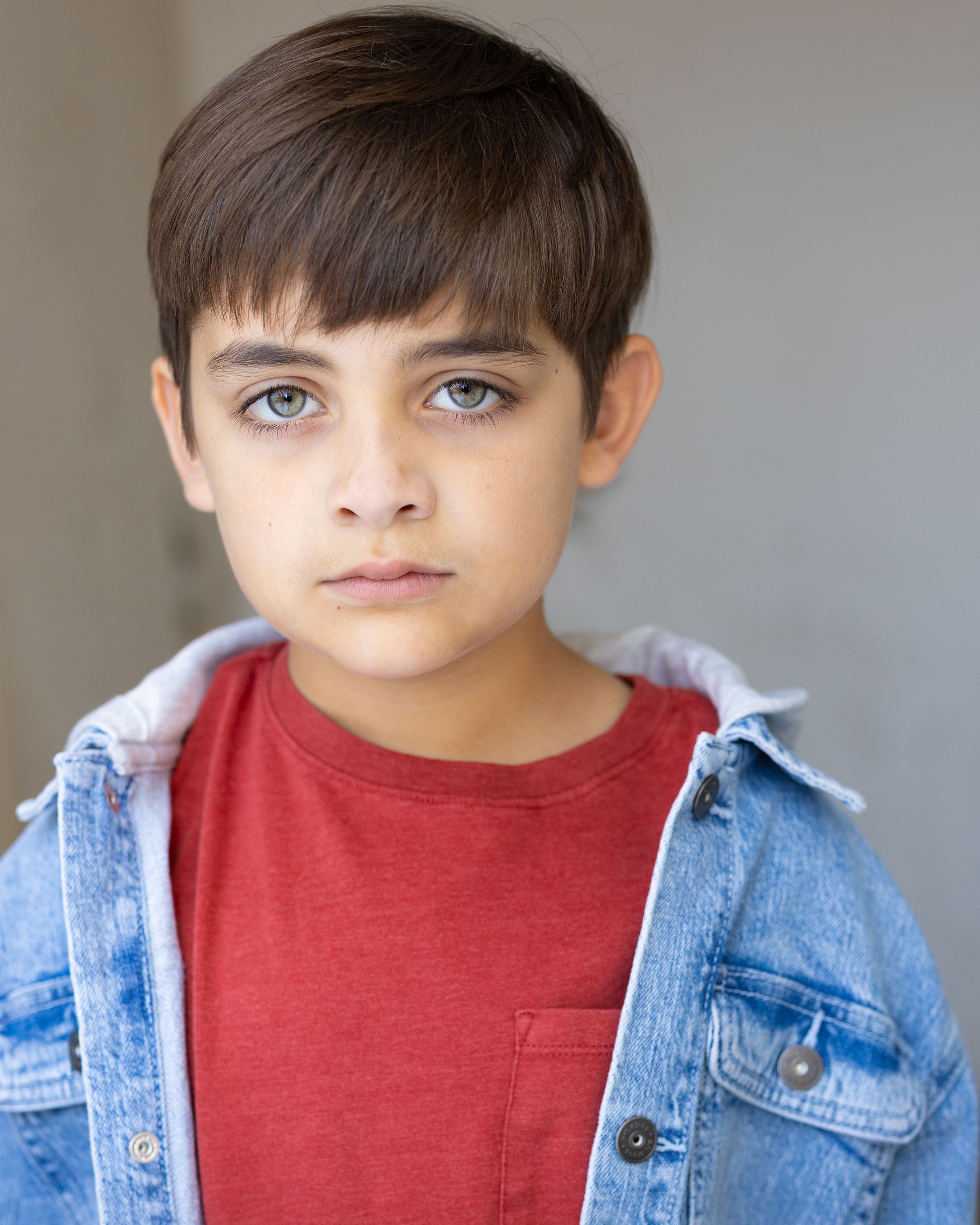 Portrait of a young person wearing a red t-shirt and denim jacket against a neutral background.