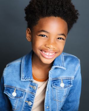 A child wearing a denim jacket and white shirt smiles warmly against a dark background.