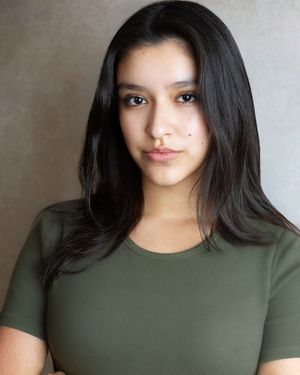 Young woman with long dark hair wearing an olive green fitted t-shirt, posing for a professional headshot photo.