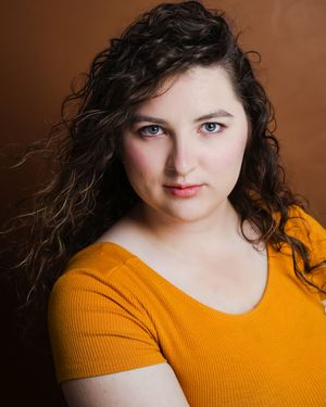 Studio portrait showing progressive movement wearing a bright orange sweater against brown background.