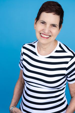 Smiling middle-aged woman with short brown hair wearing a black and white striped t-shirt against a blue background.