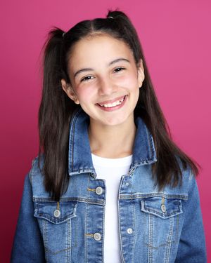 Portrait of someone in a jean jacket smiling warmly against a pink background.
