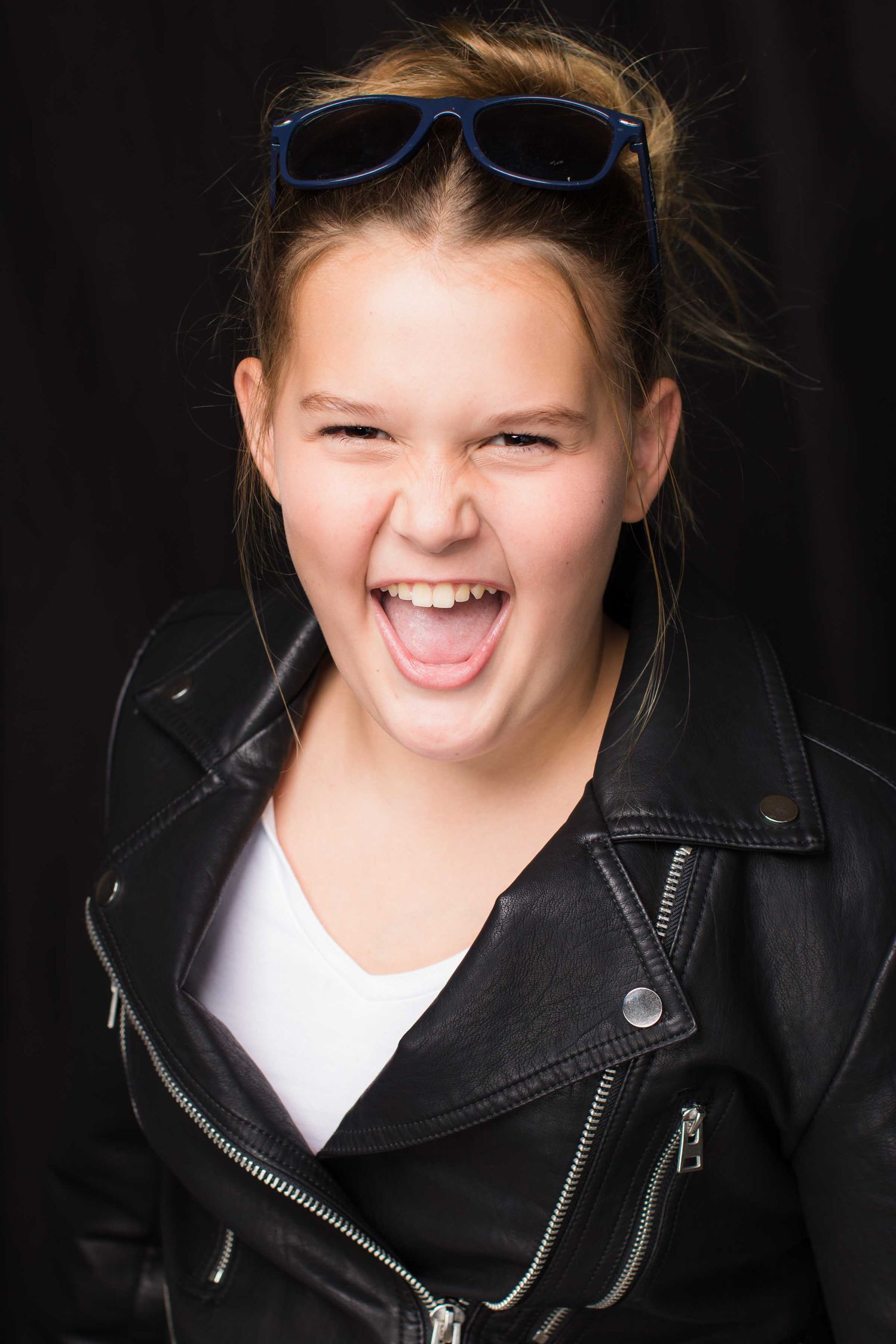 Expressive portrait of a person in a leather jacket and sunglasses with a playful expression.