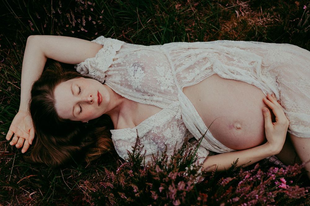 A dreamy maternity photo of an expectant mother lying among pink flowers.