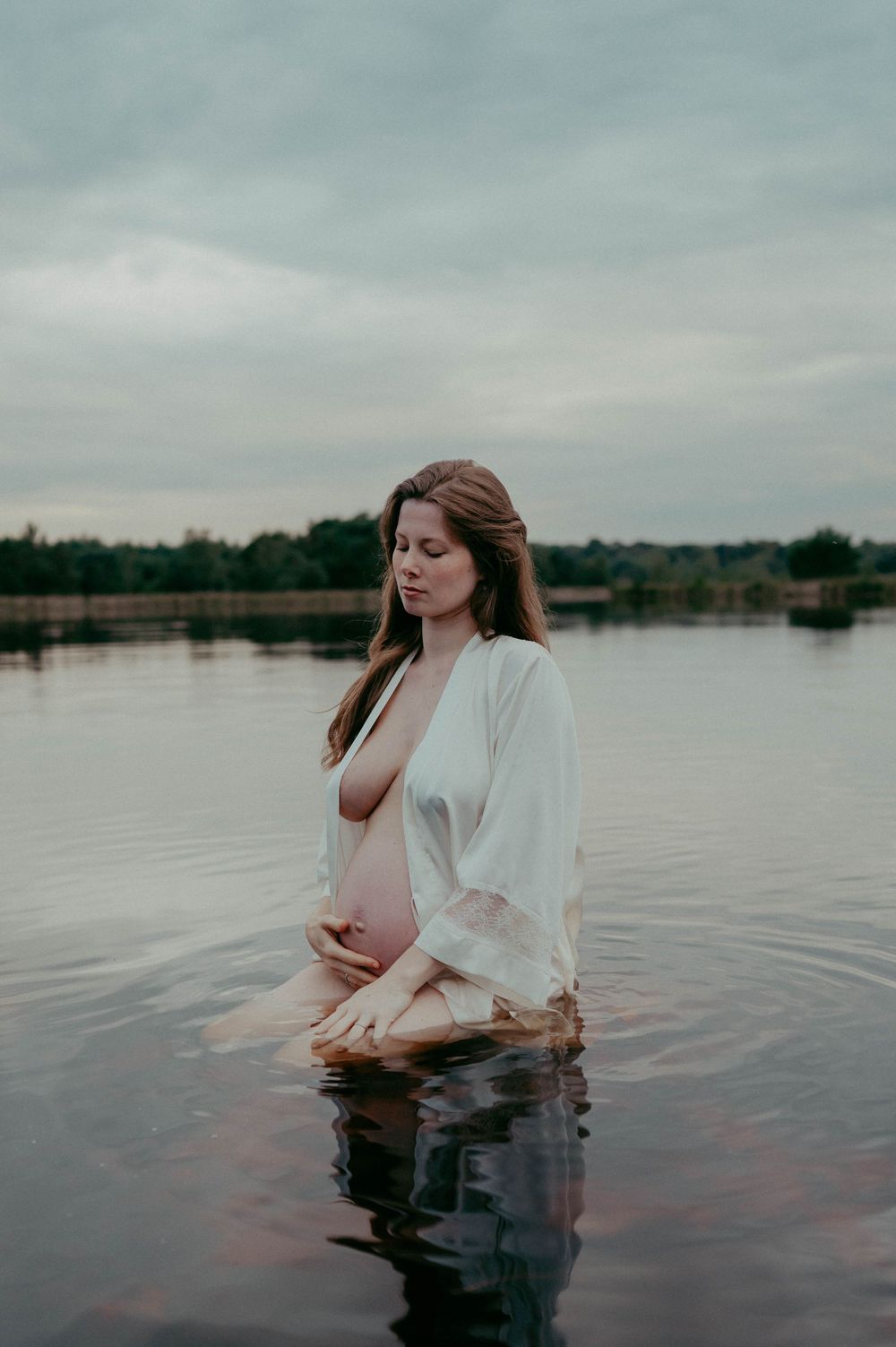 Intimate maternity moment captured in tranquil waters with soft overcast lighting.