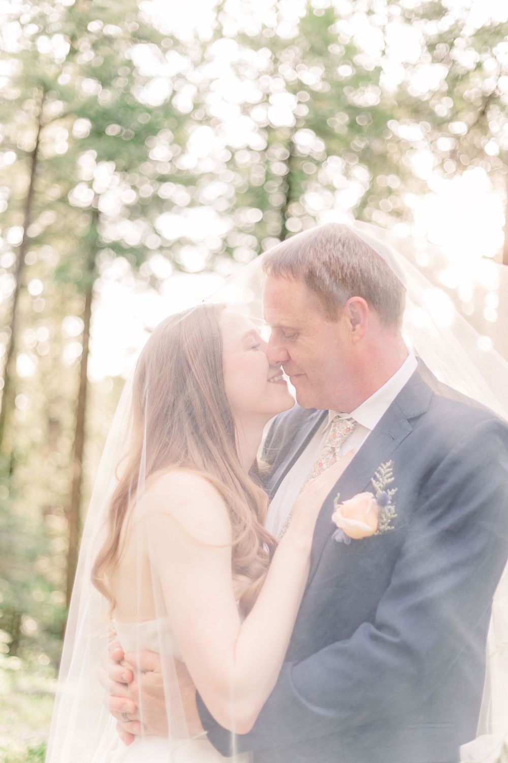 Ethereal wedding portrait of couple sharing intimate moment in sunlit forest.