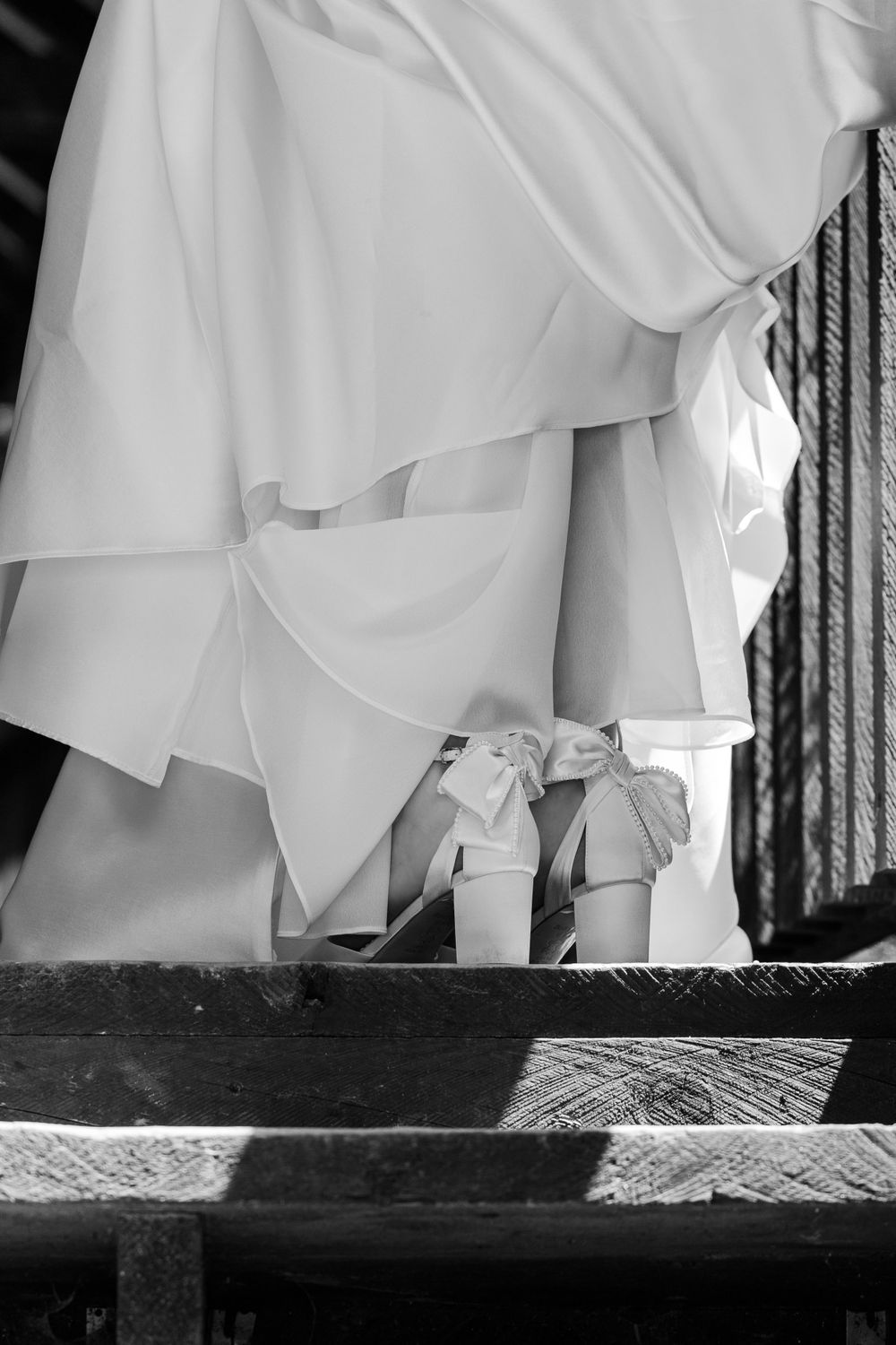 Black and white detail shot of a bride's white wedding dress and shoes on wooden steps.