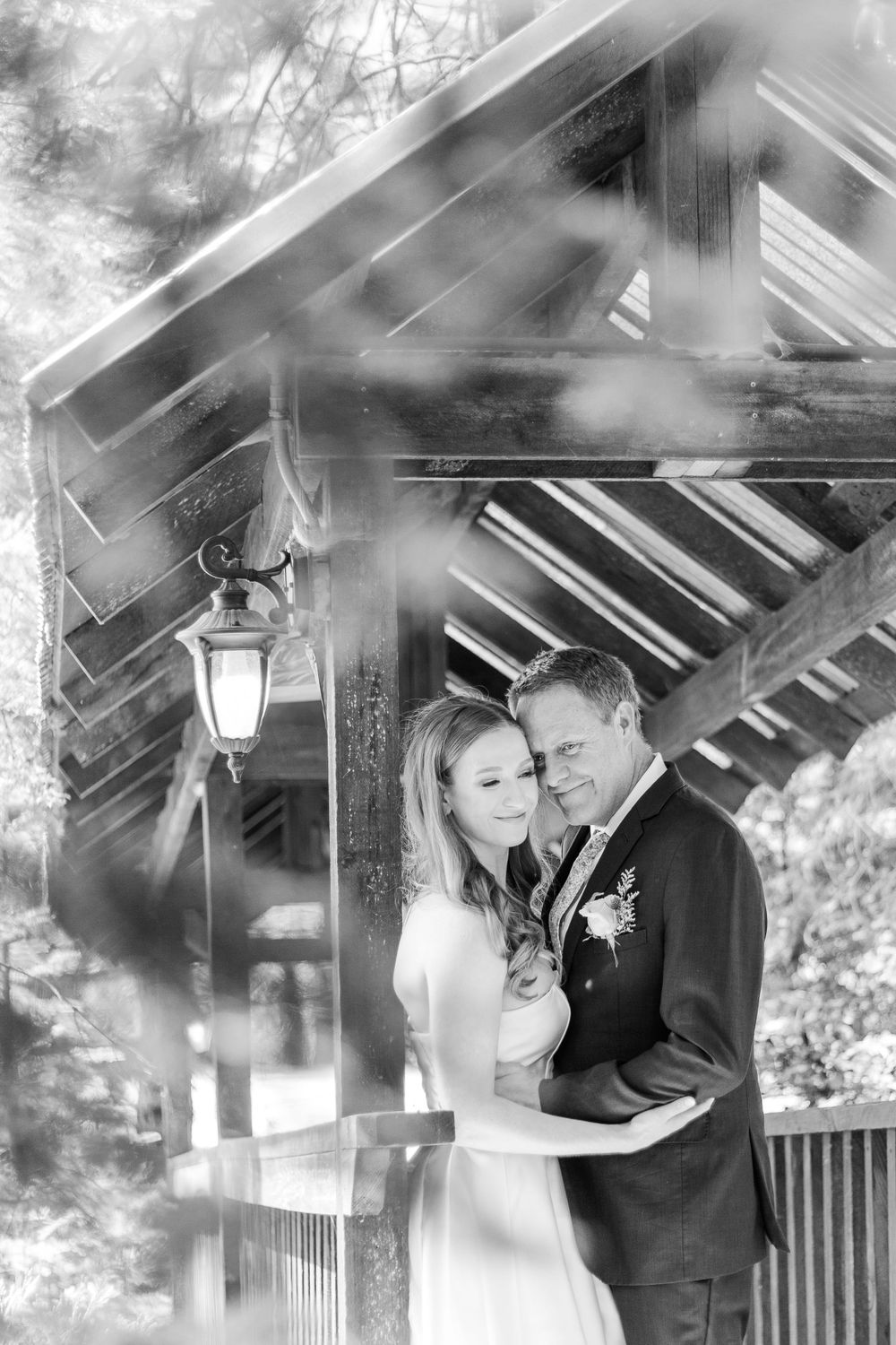 A dreamy black and white wedding portrait of a couple under a wooden pavilion.