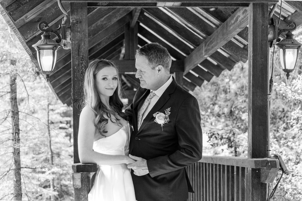 Wedding couple shares intimate moments under a wooden pavilion in a forest setting.