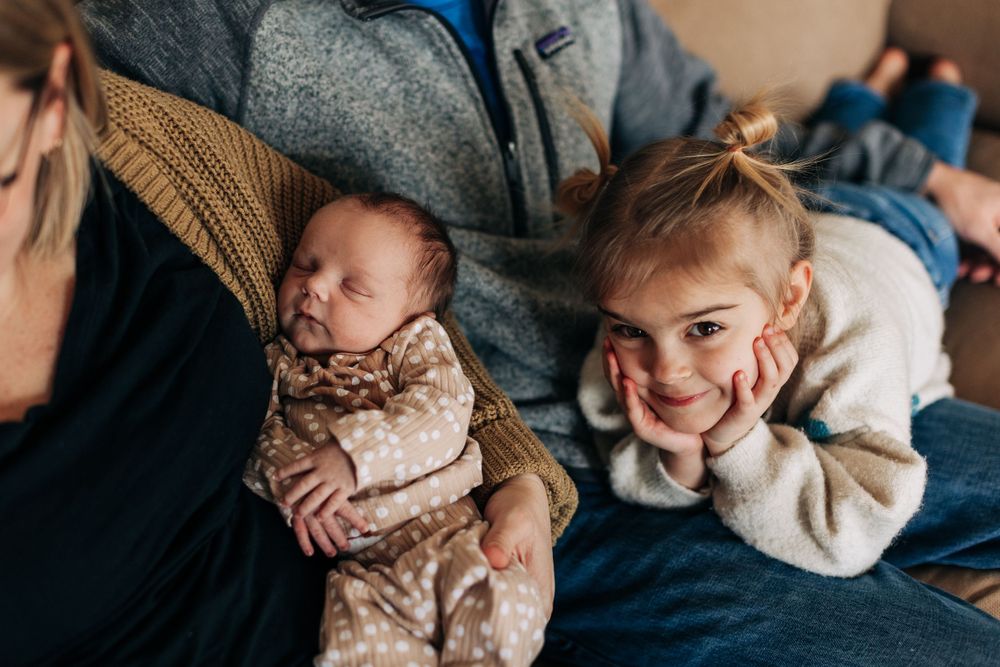 Relaxed family moment on blue couch with newborn and older sibling.
