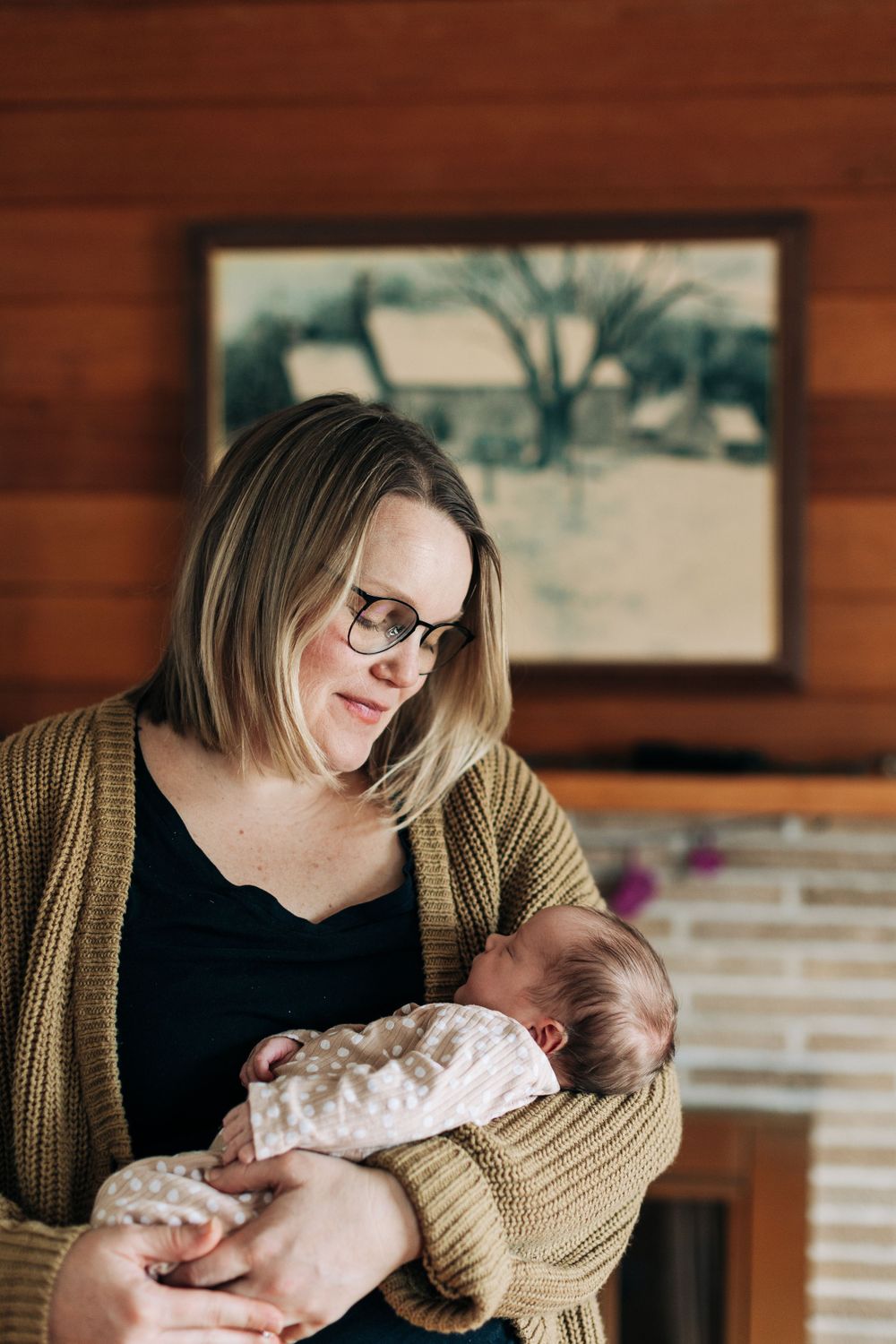 Tender moment of affection while holding a swaddled newborn in a brown cardigan.