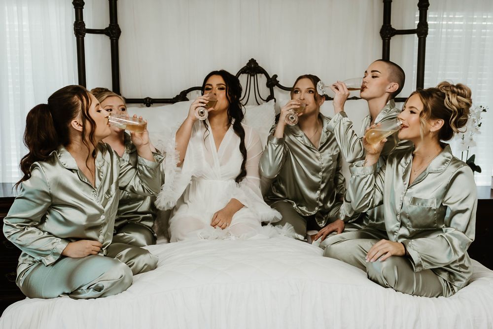 Wedding party in silk robes laughing together on white bed.