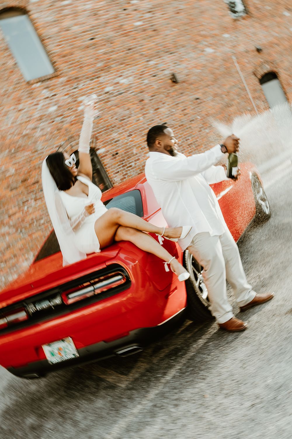 Couple in white outfits lounging on red vintage car during photo session.