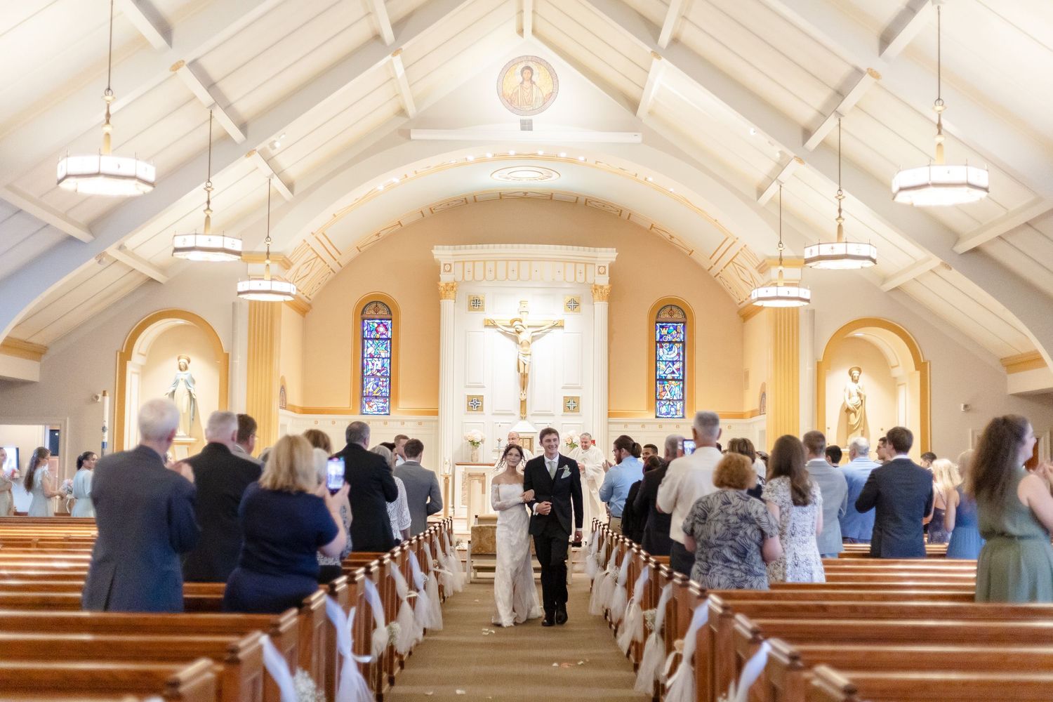 Bride and groom walk down the aisle of a beautiful white chapel during their wedding ceremony.