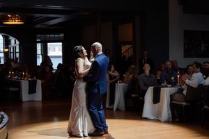 Bride and groom share their first dance at an elegant wedding reception with candlelit tables and guests in background.