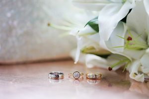 Three elegant wedding rings displayed on a marble surface beside a bouquet of white lilies.