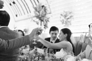 Black and white wedding reception toast with bride and guests raising champagne glasses at elegant floral table.