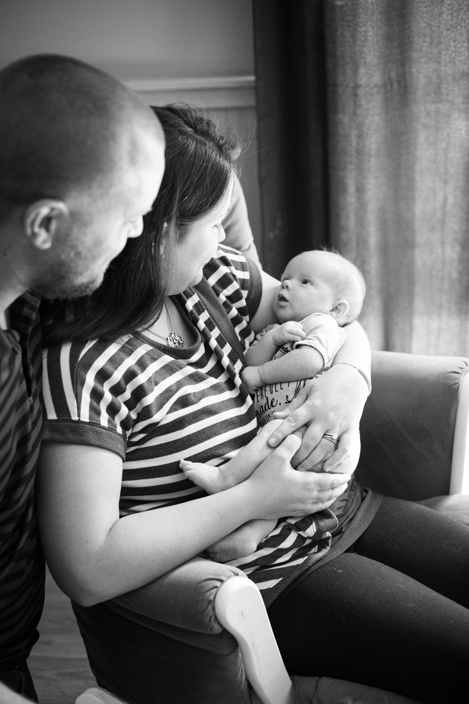 New parents in striped shirts lovingly gazing at their newborn baby in black and white.