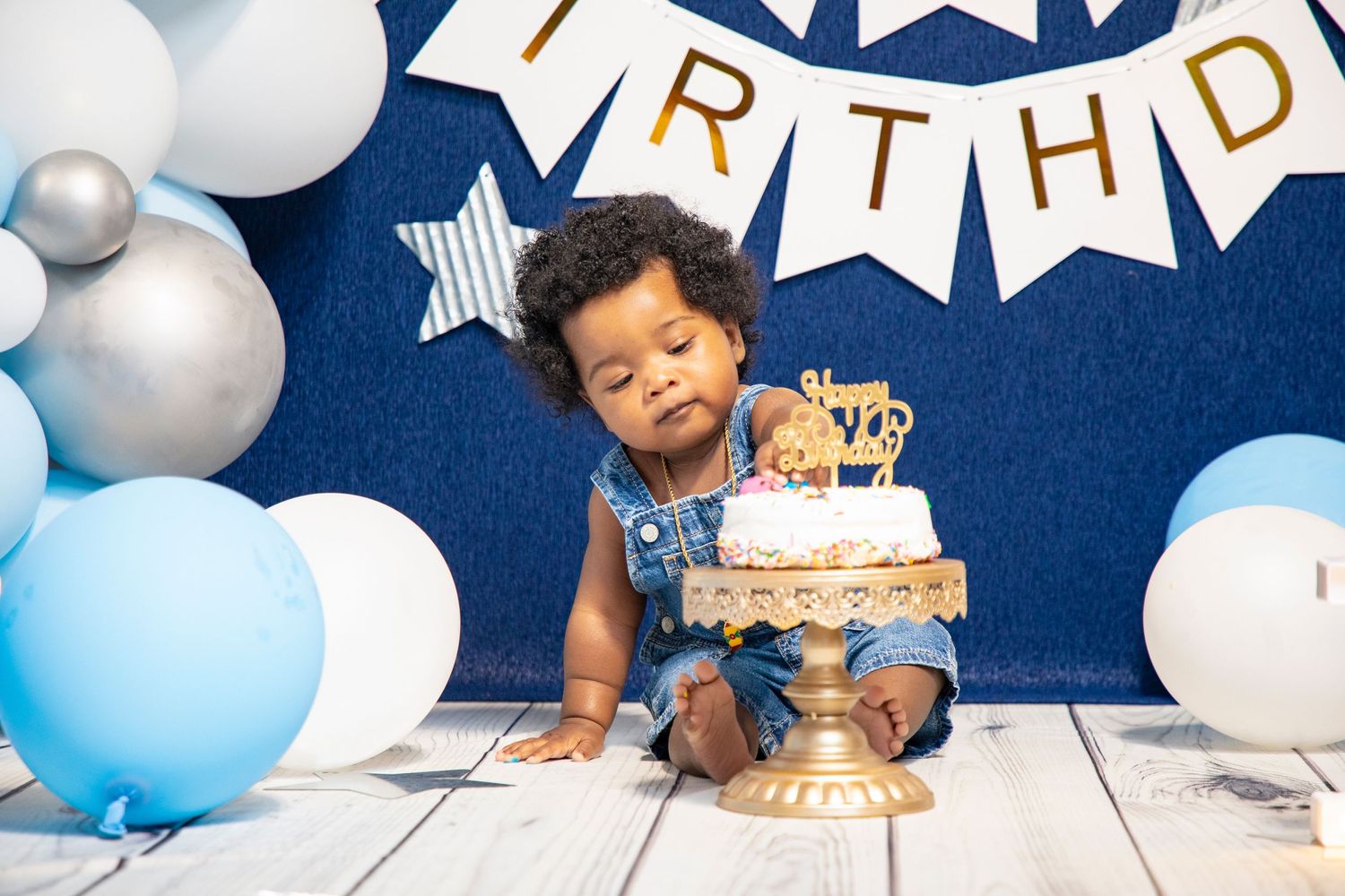 Baby's first birthday setup with blue and white balloons, stars, and golden crown decorations.