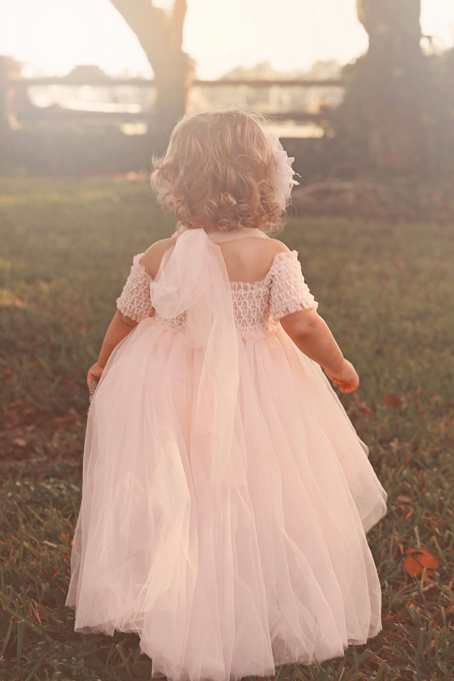 A small child in a flowing pink tulle dress walking in a sunlit garden.