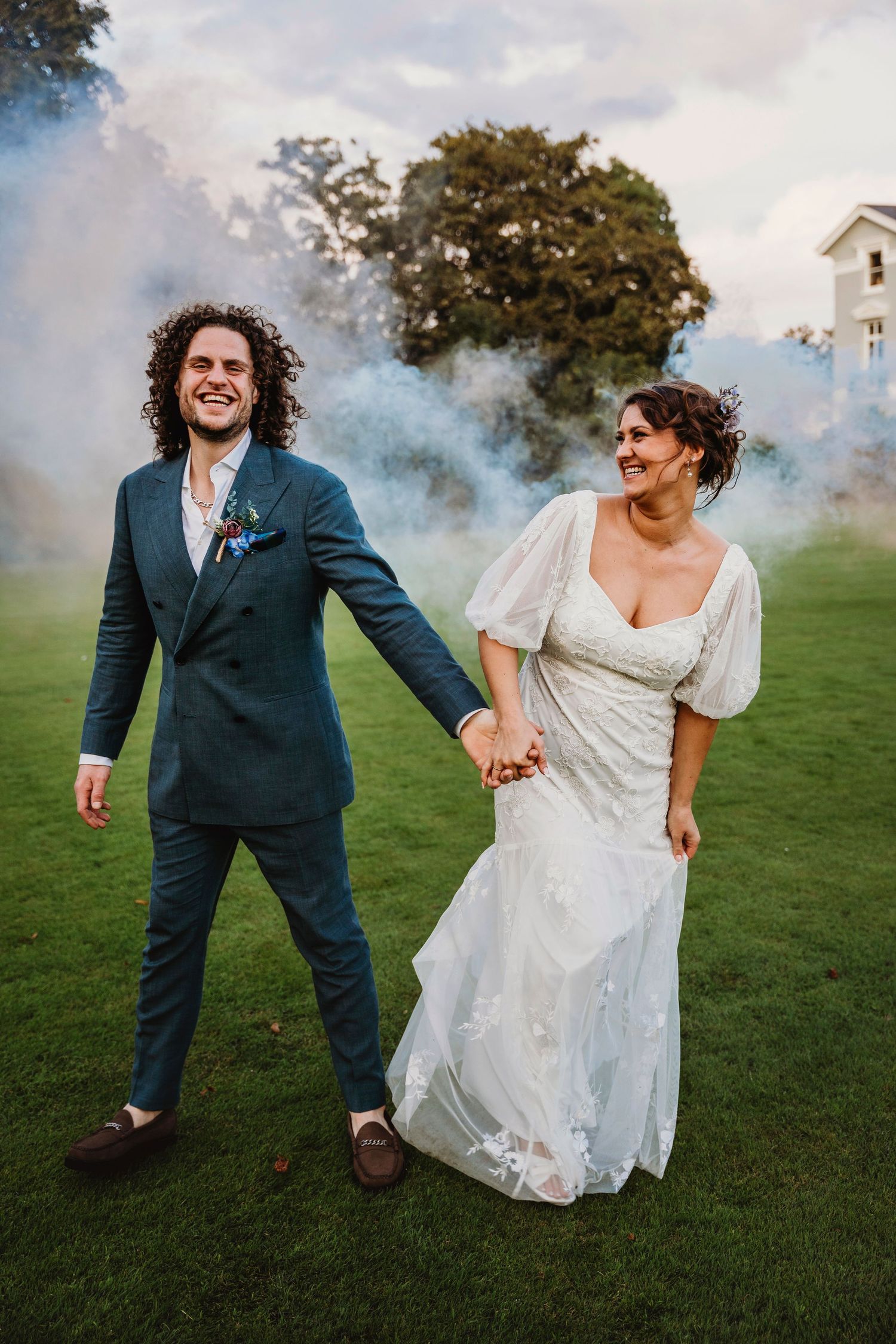 Wedding couple dancing and twirling on green grass in formal attire.