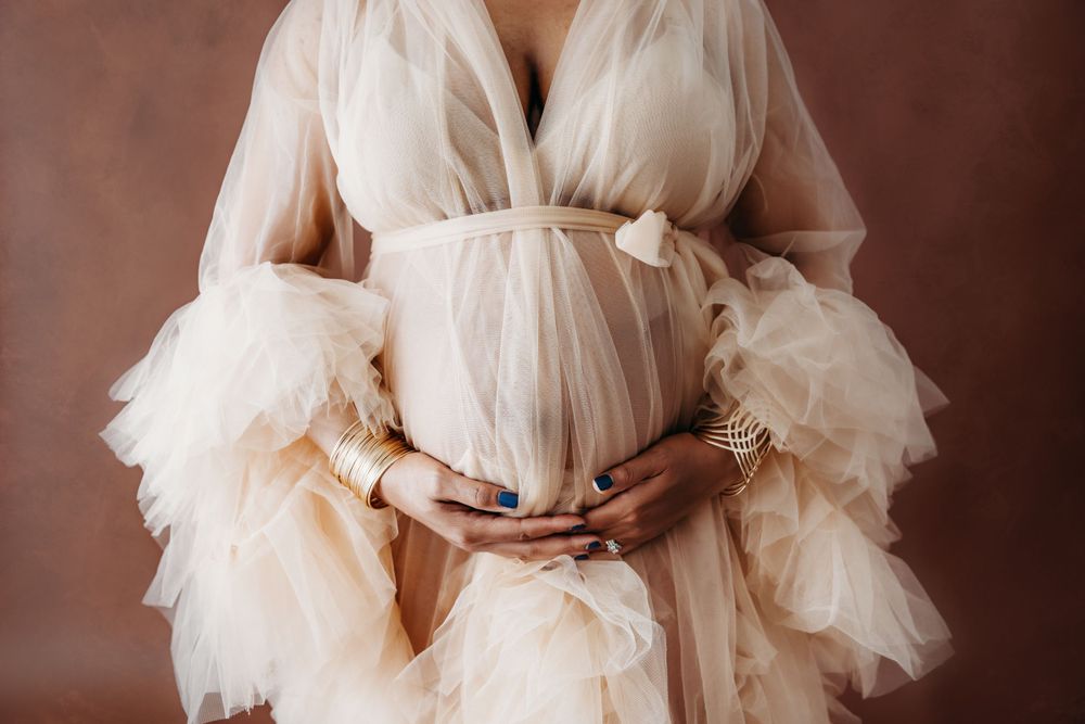 Ethereal maternity photos featuring flowing white tulle dress against dark backdrop.