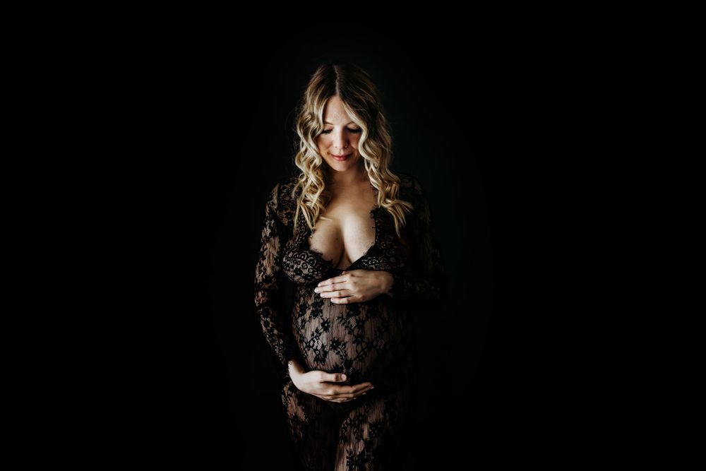 Artistic boudoir photography in black lace against dark background with moody lighting.