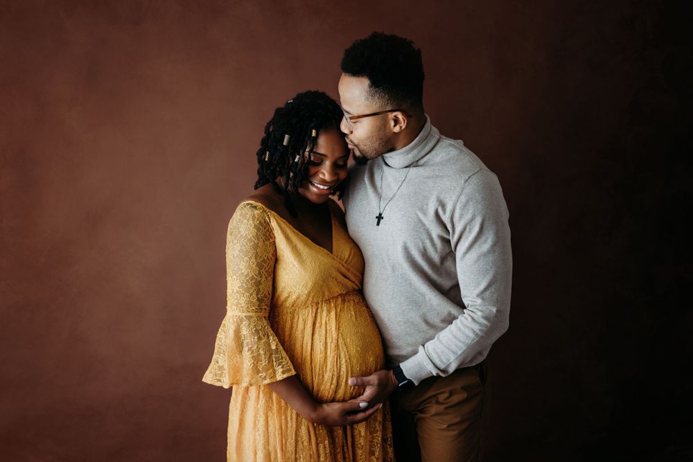Moody maternity photography session with dark brown studio backdrop.