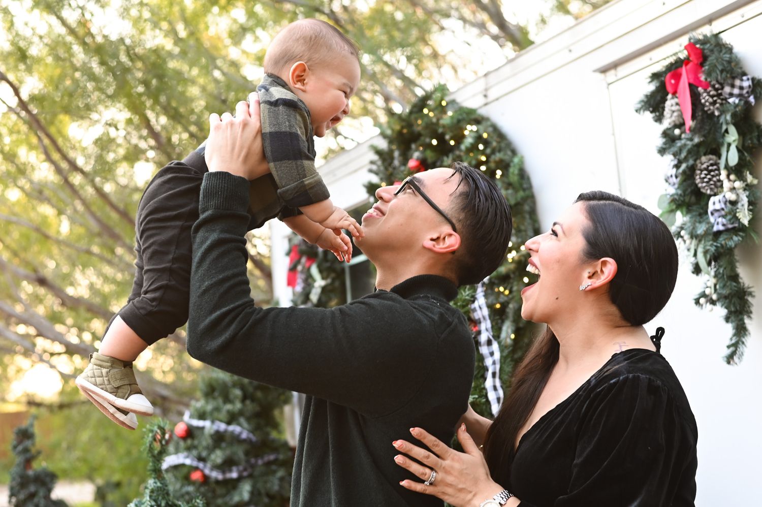 A joyful holiday moment with a baby being lifted in the air outdoors.
