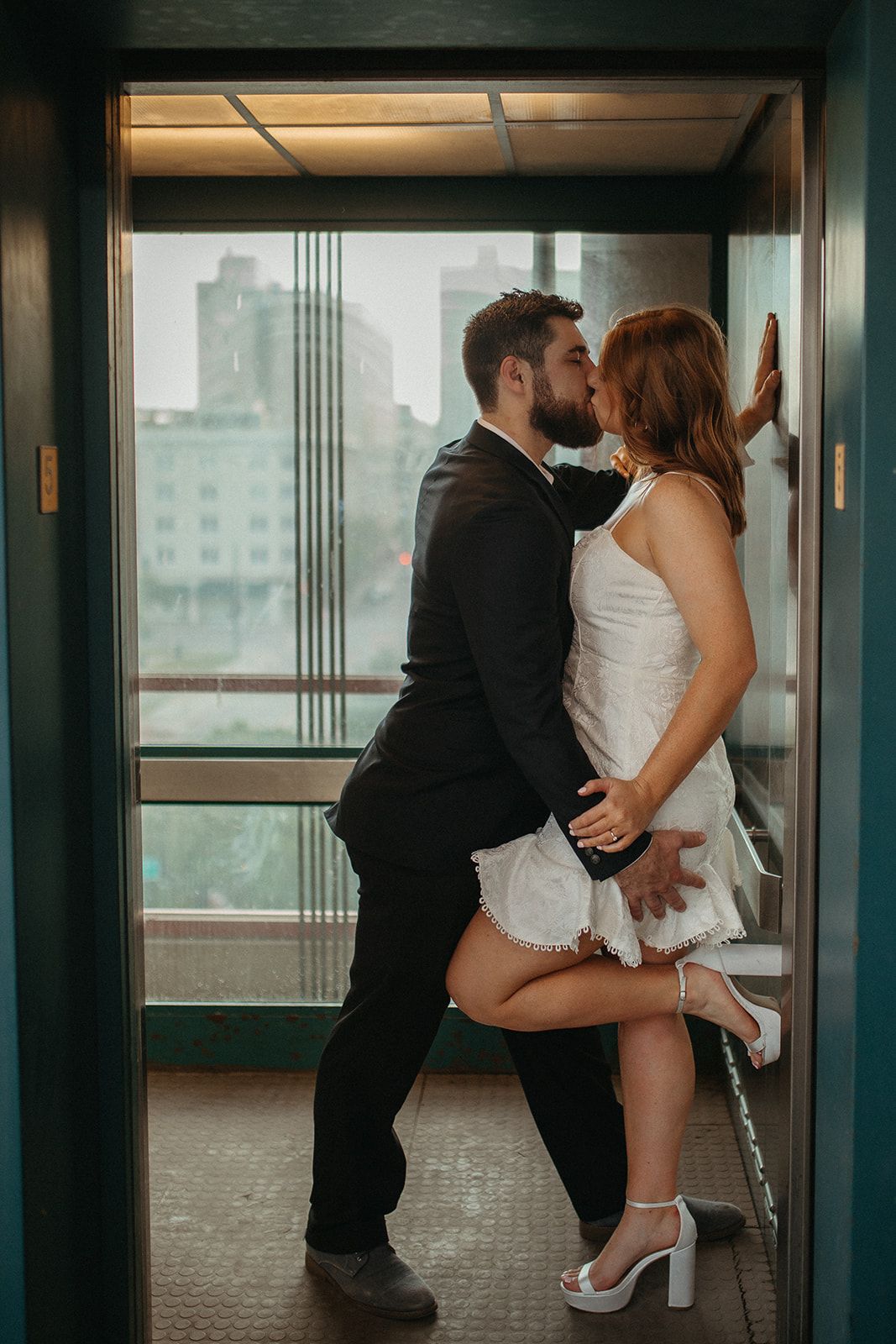 A couple sharing a passionate moment in an elevator wearing formal attire.