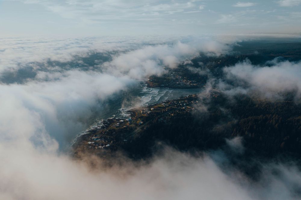 Aerial view of misty mountains and clouds stretching across a vast landscape at sunrise.