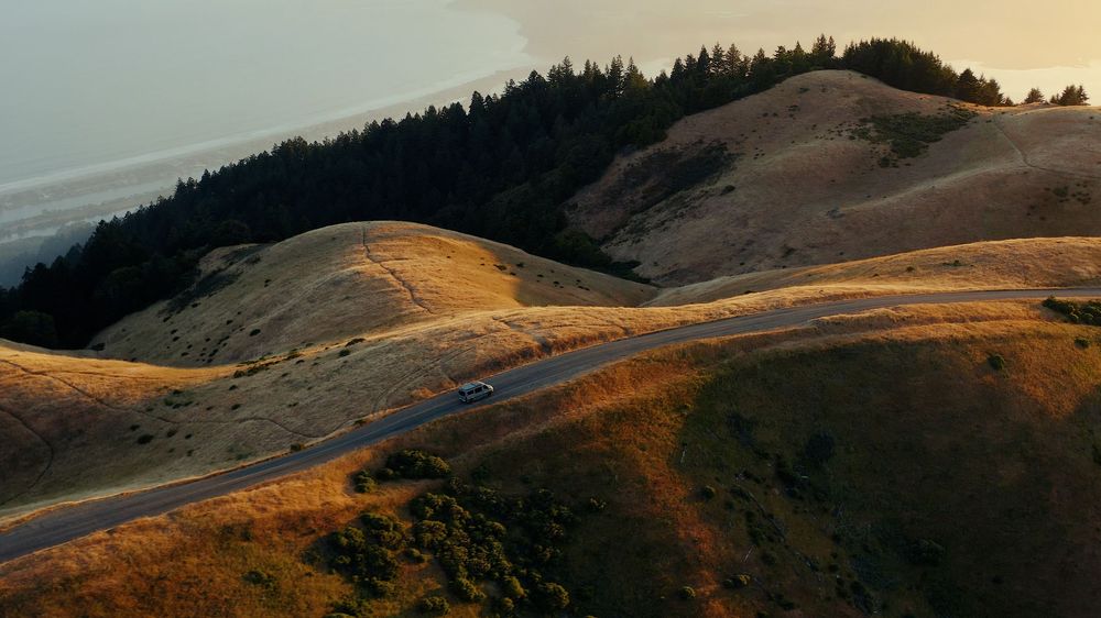 Winding mountain road curves through golden rolling hills at sunset.