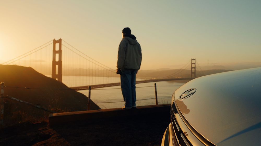 Silhouette against Golden Gate Bridge at sunset with car in foreground.