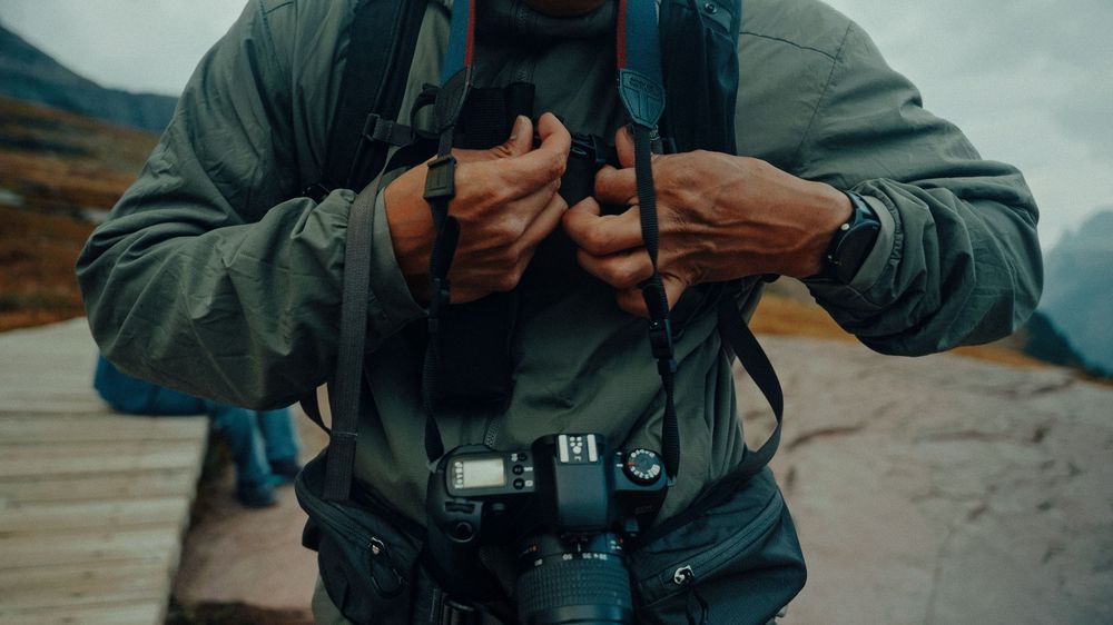 A person wearing a gray jacket operates a camera while taking photos in an outdoor setting.