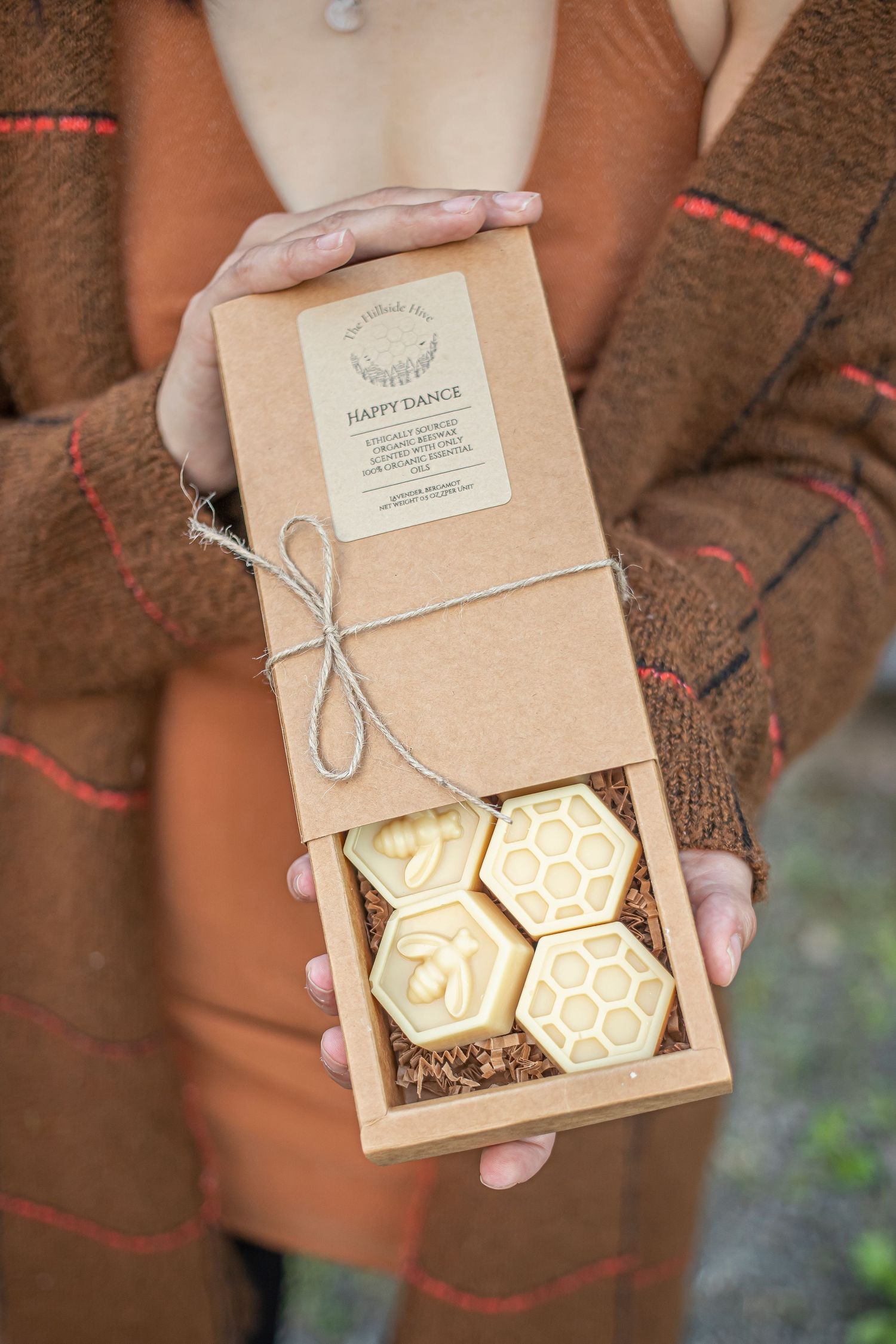 Hands holding an open kraft box revealing decorative honeycomb-shaped soaps inside.