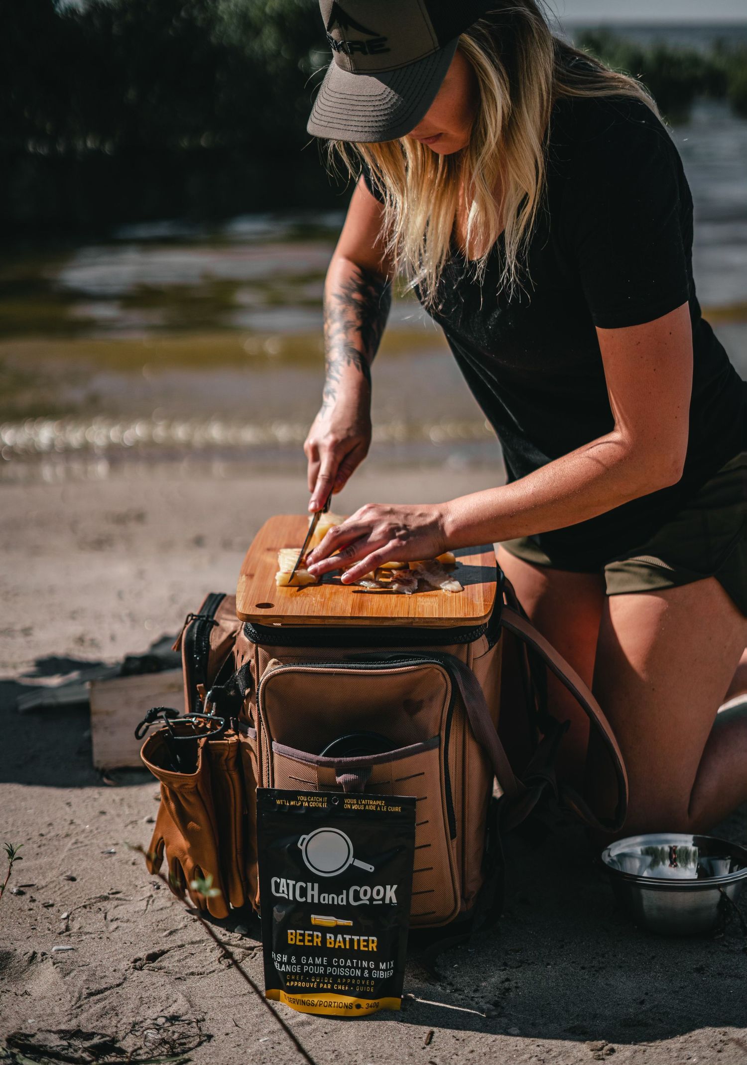 Person preparing food on wooden cutting board with seasoning container on beach.