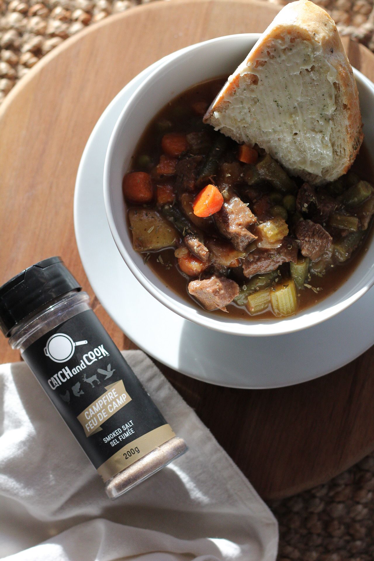 Bowl of hearty stew with bread and Catch and Cook seasoning container.