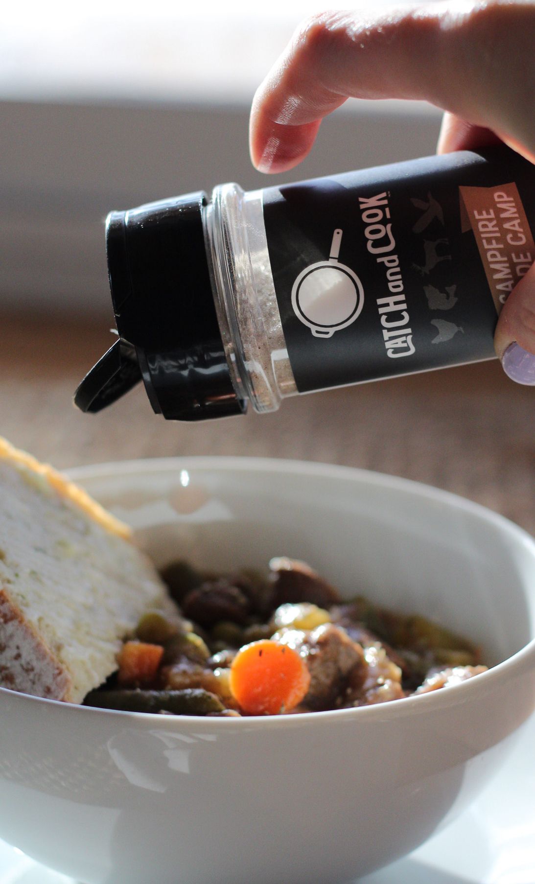 Seasoning being sprinkled from Catch and Cook container onto a bowl of stew.