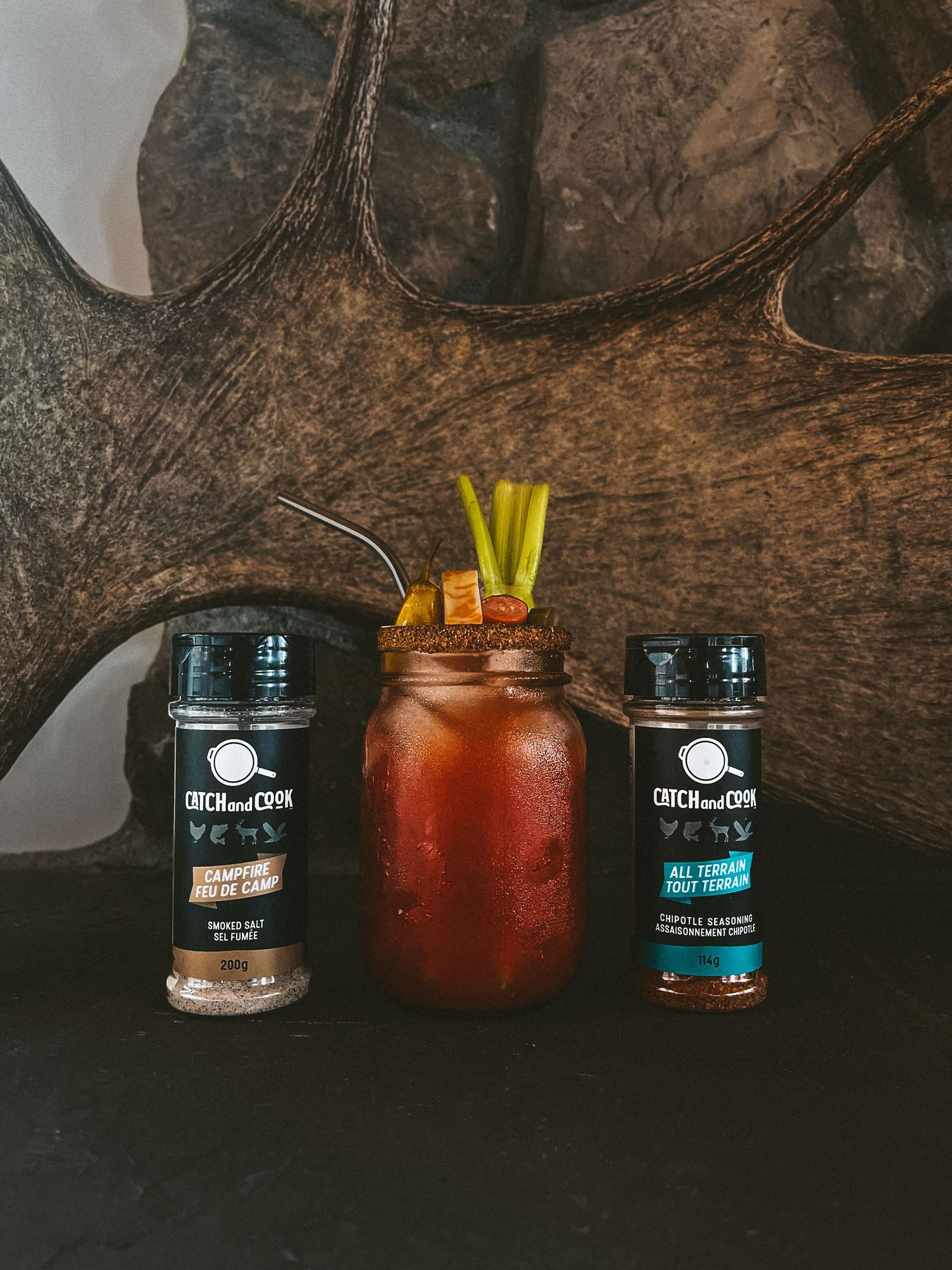 Bloody Mary cocktail with celery garnish flanked by two seasoning bottles.