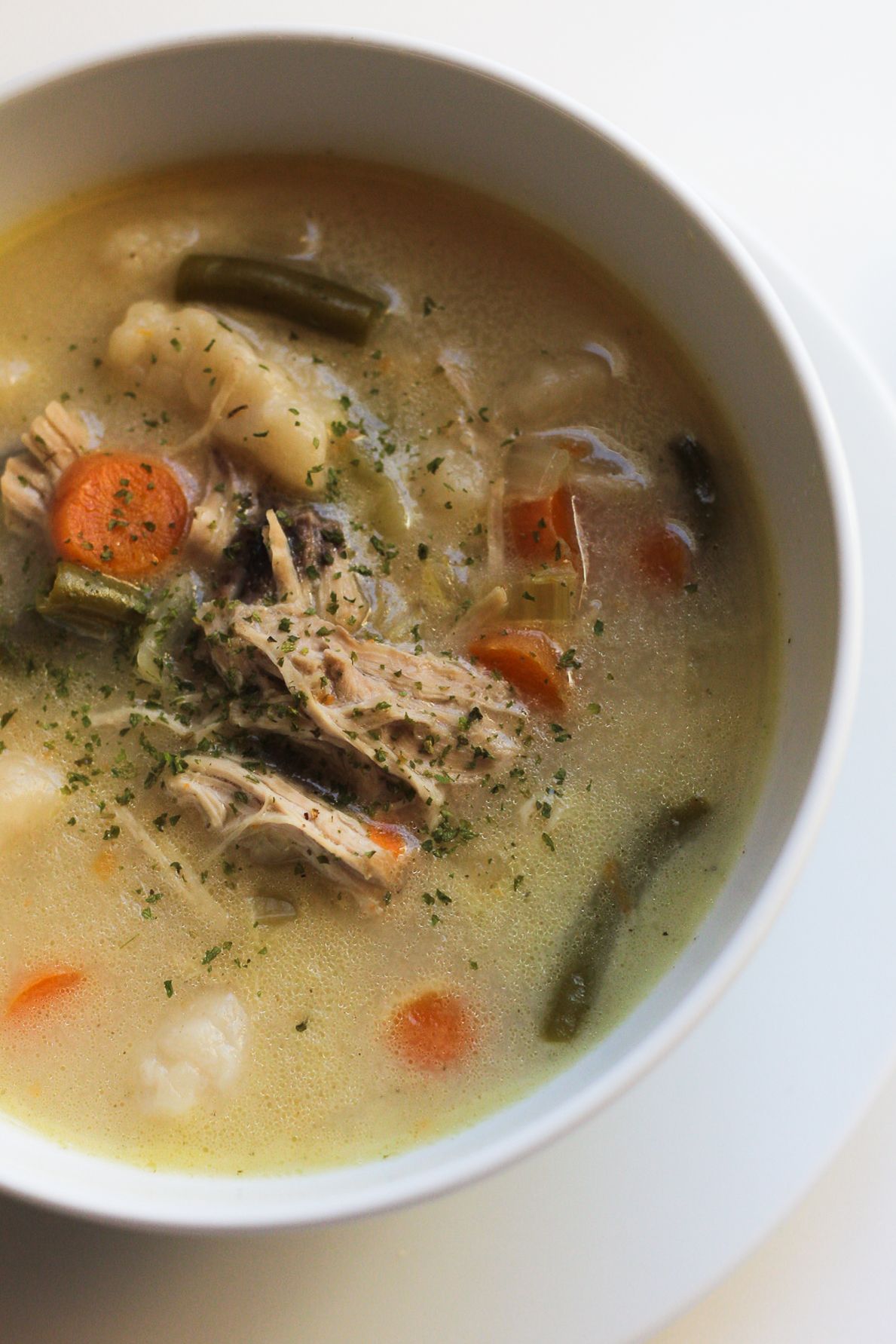 Homemade chicken soup with vegetables and herbs in white bowl.