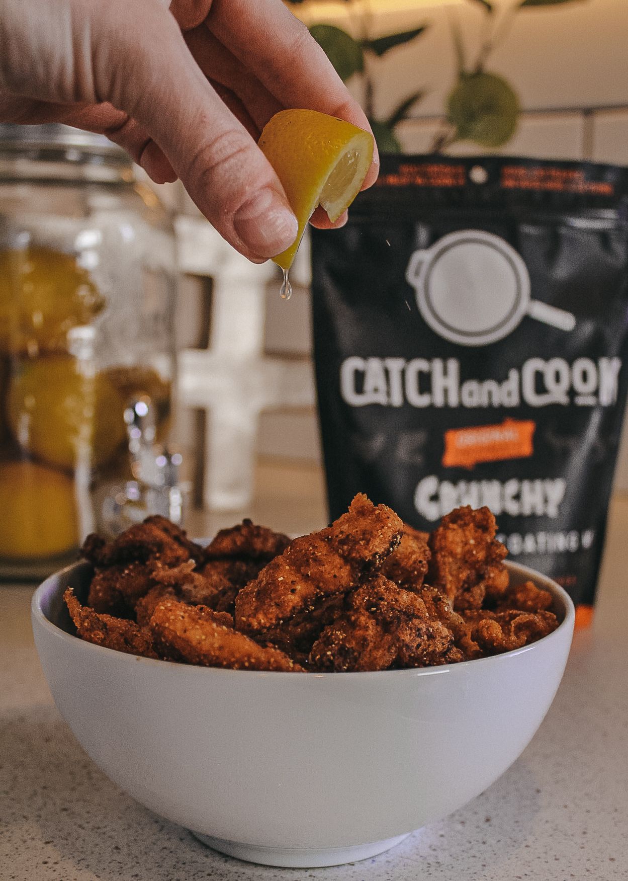 Squeezing lemon over spicy chicken wings in white bowl with Catch and Cook seasoning package.