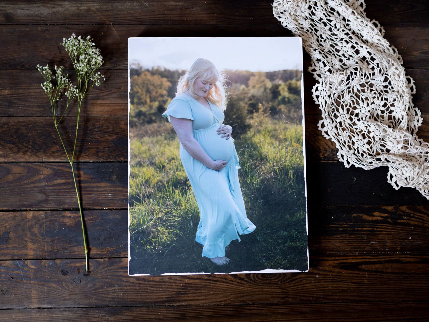 Maternity photo displayed on rustic wooden surface with lace and dried flowers.