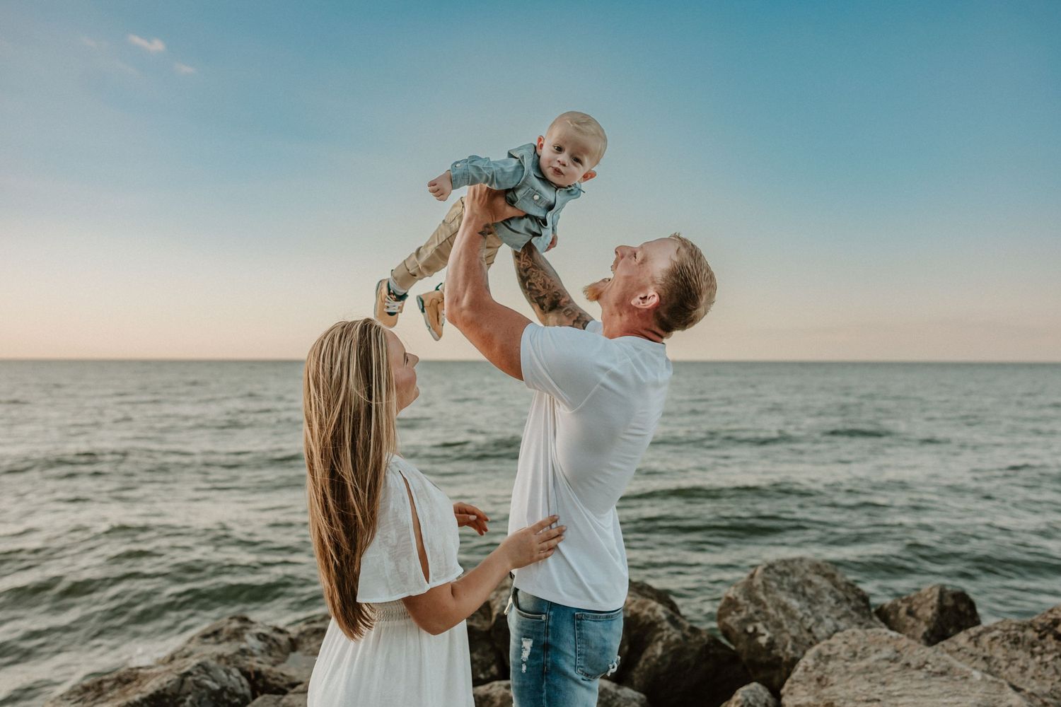 Family playing together on rocky beach shore during sunset by the ocean.